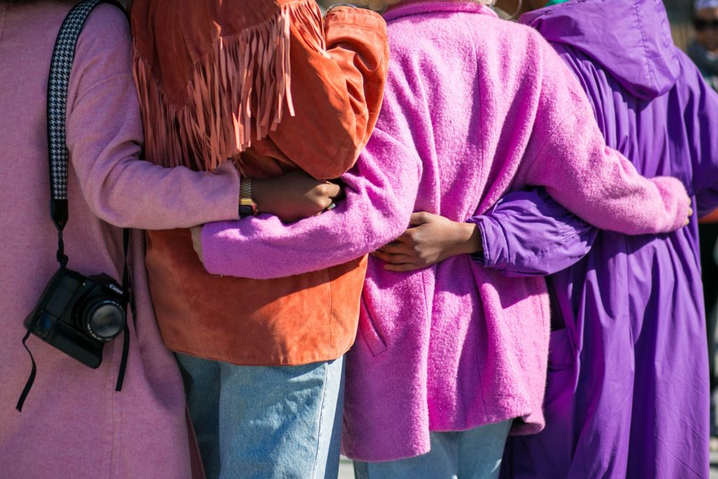 Four people in brightly coloured coats hugging to show connection through market positioning