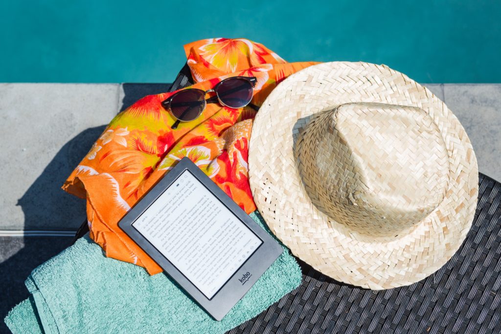 Sunglasses, sunhat and an e-book by the pool.